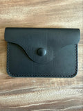 A small black leather card holder or wallet with a flap closure and snap button, photographed from above on a wooden surface.