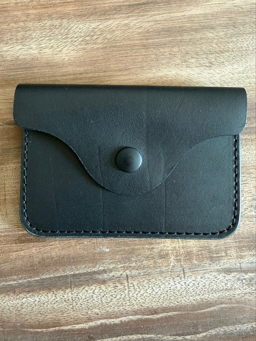 A small black leather card holder or wallet with a flap closure and snap button, photographed from above on a wooden surface.